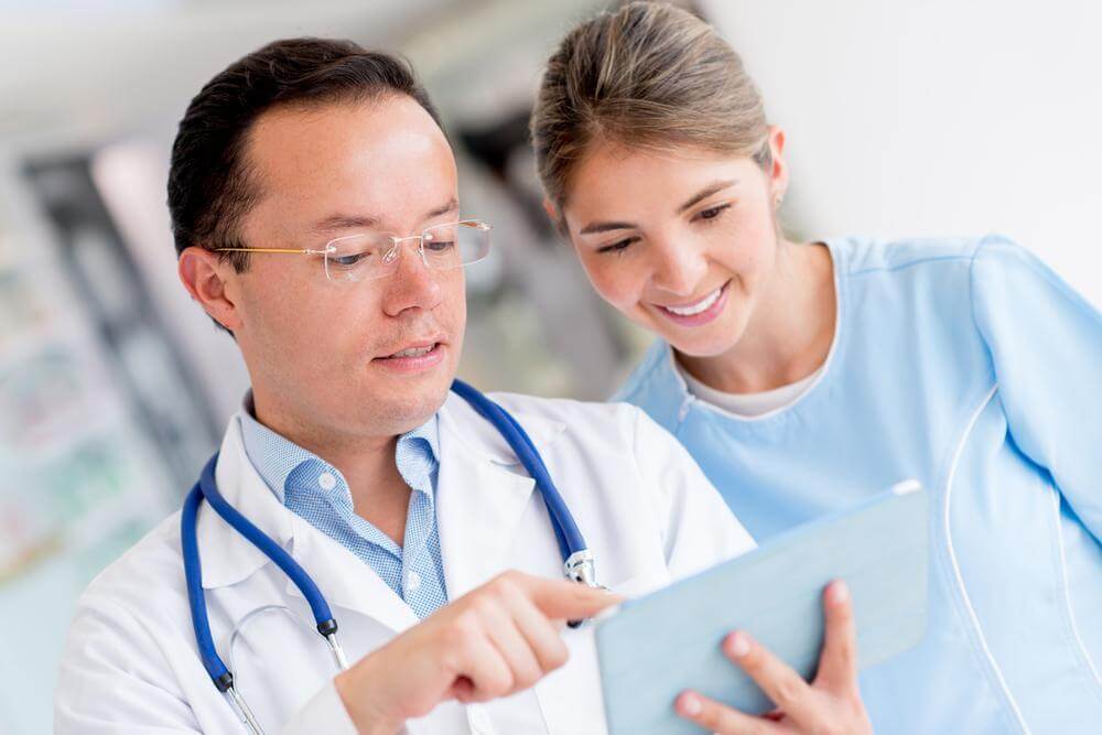 A doctor and nurse reviewing documents on a laptop.