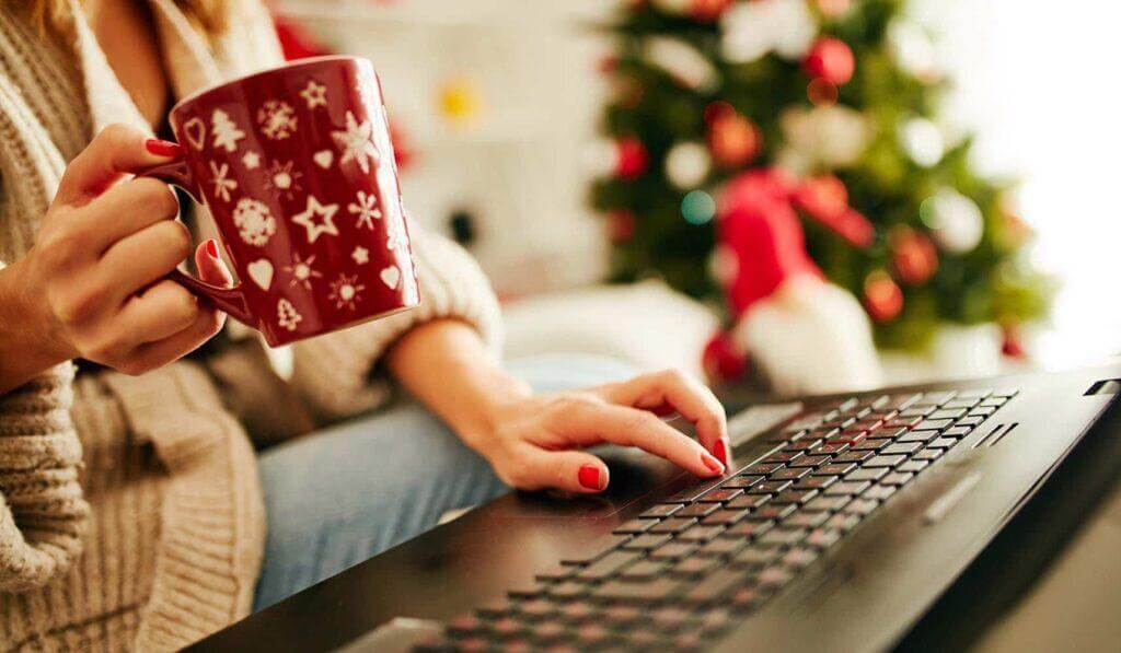 Woman holding holiday coffee mug while using laptop.
