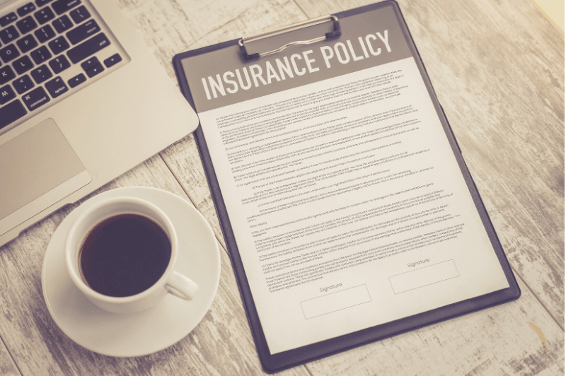 Insurance policy documents next to coffee cup and computer.
