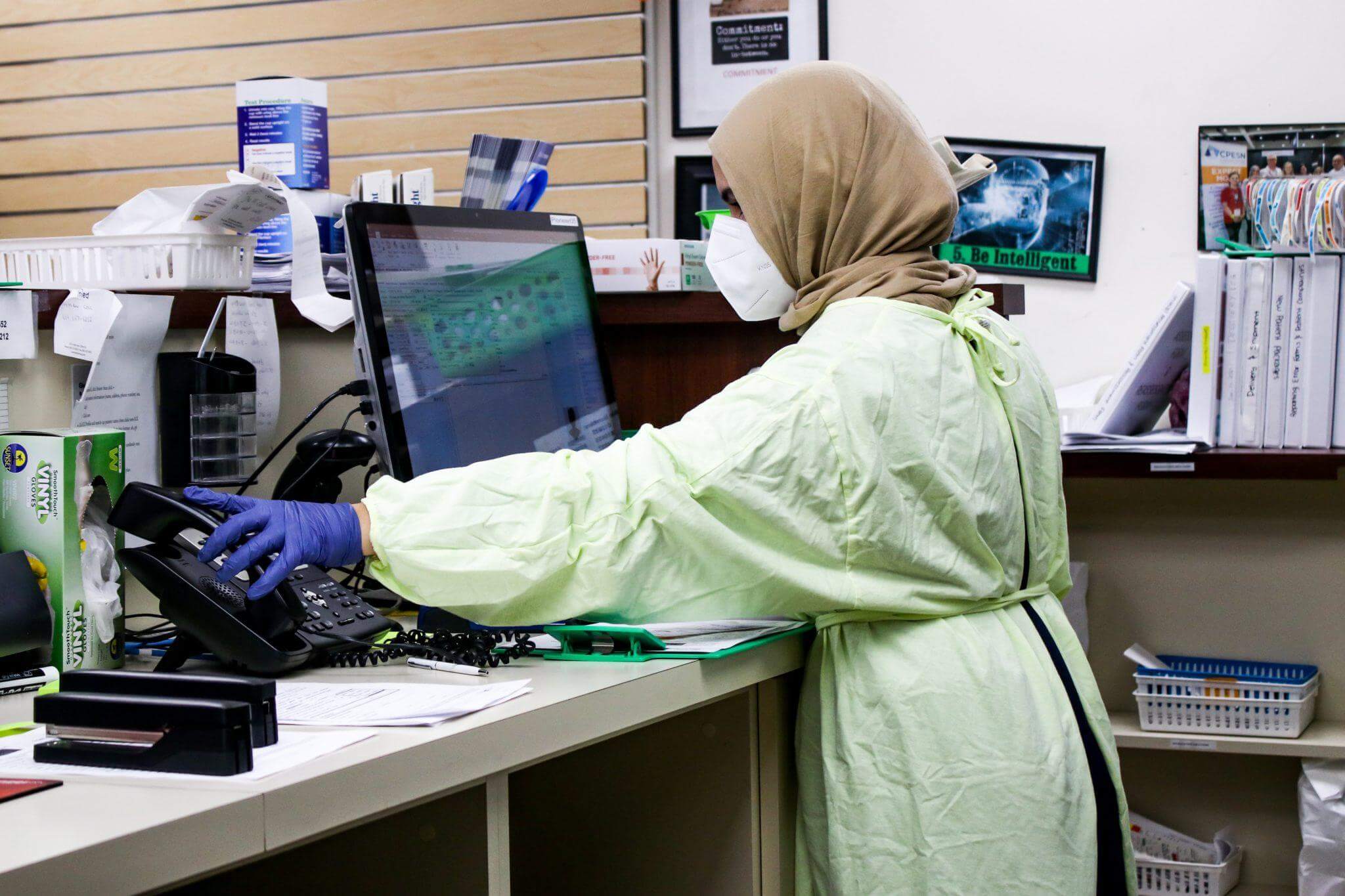 Pharmacy worker reaching for telephone while workinig on a laptop.