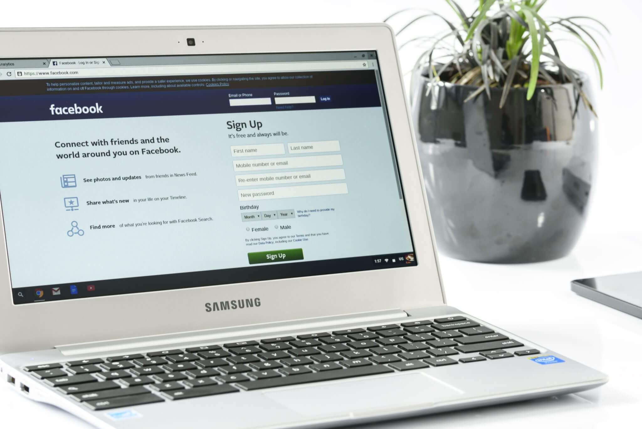White samsung laptop computer with Facebook login screen loaded near black ceramic plant vase.