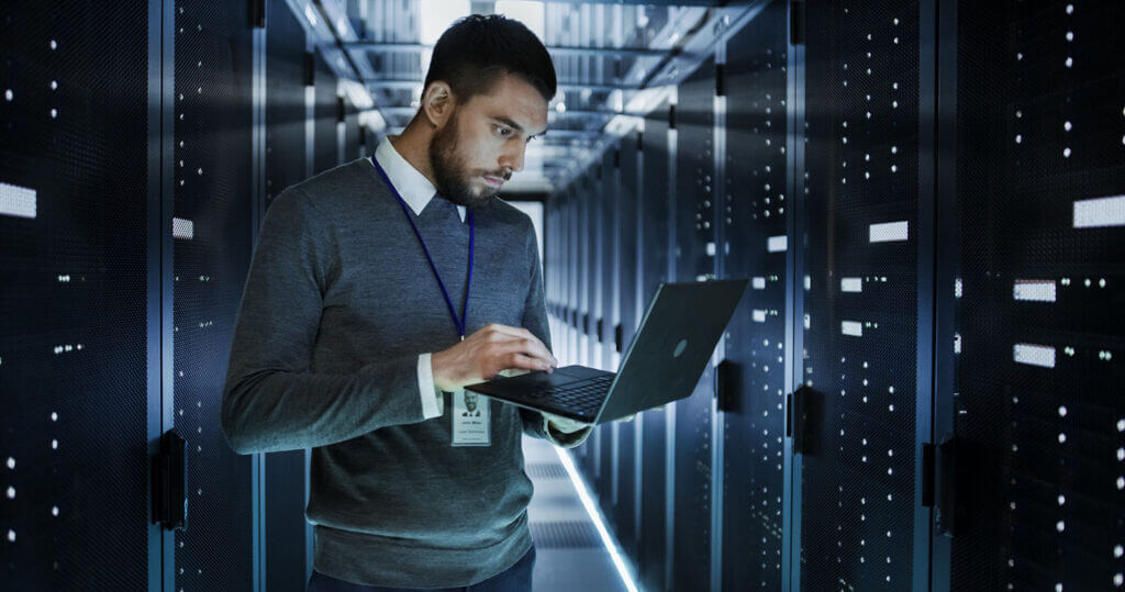 IT worker on computer in a network closet.