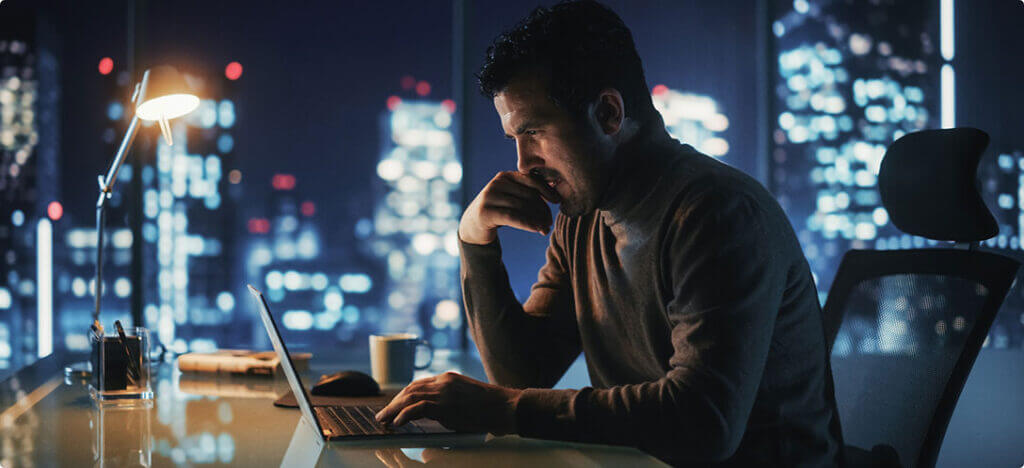Man sitting at a desk in a corporate office overlooking a night city sklyine.